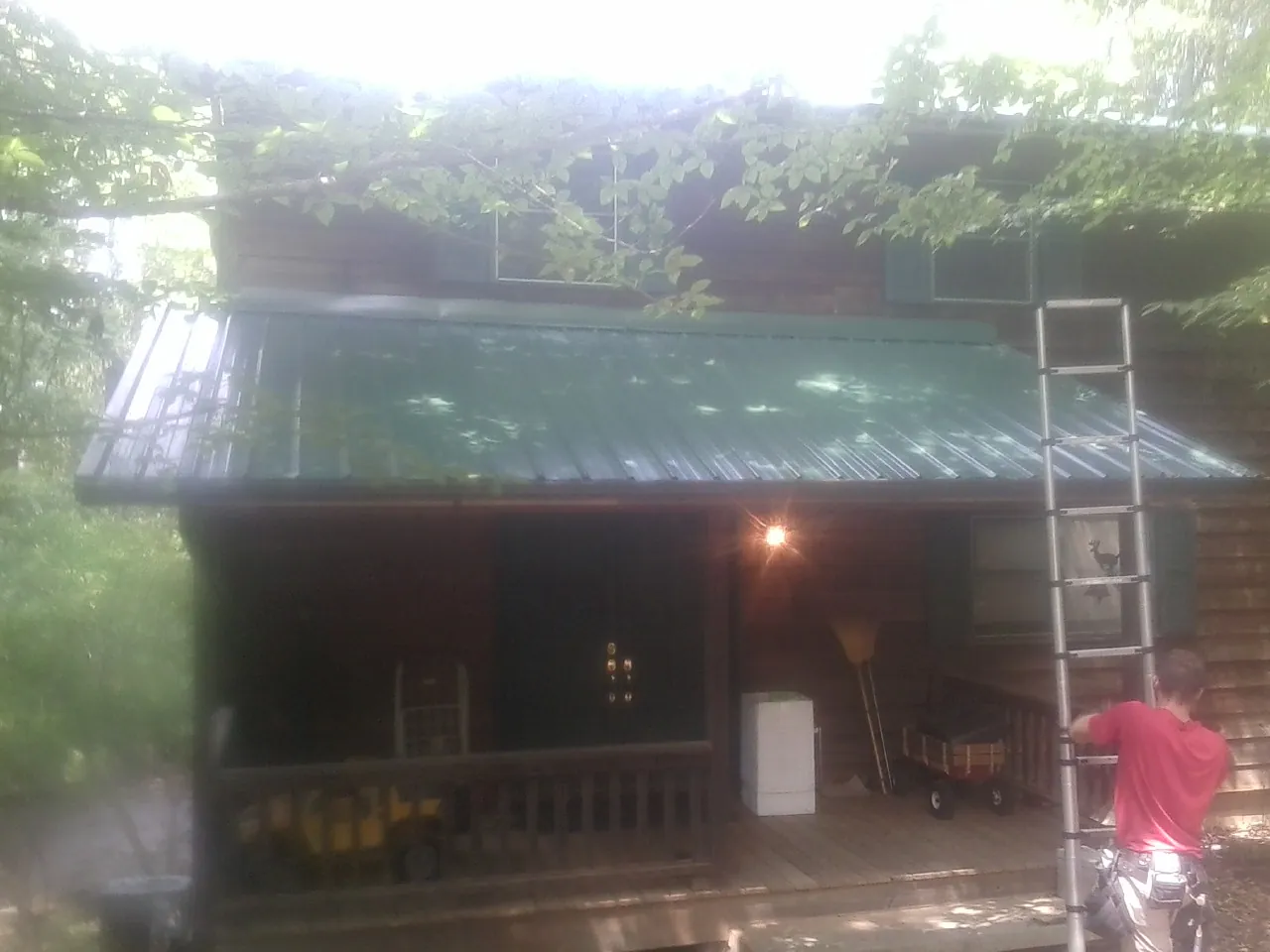 Worker on a ladder at the green porch roof of a wooded cabin in Williamsburg